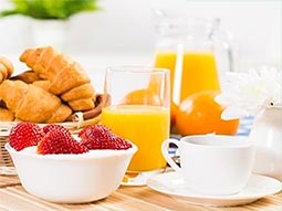 A bowl of pastries and strawberry's alongside a glass of orange juice on a table 