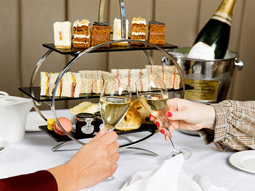 Two people clinking prosecco glasses in front of afternoon tea at DoubleTree by Hilton