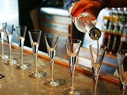 Vodka getting poured into various glasses, on a bar