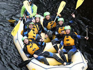 A group of people on a white water raft with paddles in hand