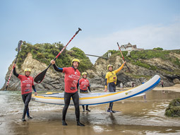 Four people on the beach holding ores and a SUP in Newquay