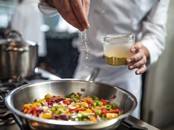 A chef seasoning a colourful dish on a stove