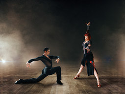 Two people salsa dancing with a dramatic dark background