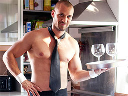 A topless man wearing nothing but a tie and apron with two drinks on a tray
