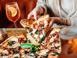 Someone pulling away a large slice of pizza with drinks on the table at Box