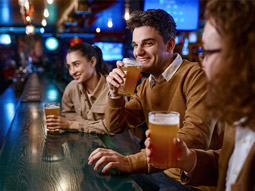 Three people drinking pints at a bar
