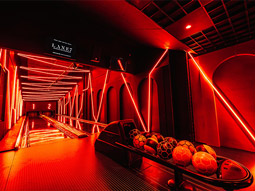 A red neon lit room with bowling alleys and balls in at Lane 7 