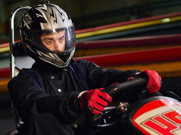 A man with a helmet and gloves on racing on an indoor go kart track