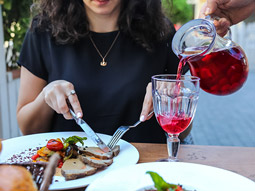 A glass of sangria being poured while a woman enjoys her meal