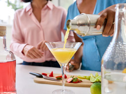 A cocktail being poured out into a martini glass