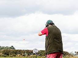 A man aiming a shotgun into the sky, with an orange clay visible