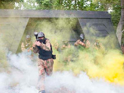 A man appearing out of some smoke with a paintball gun in hand