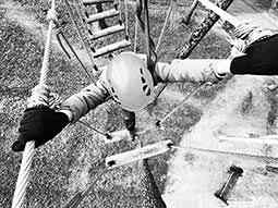 Black and white image of a woman walking along a rope bridge above the ground