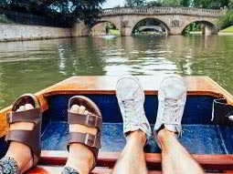 A woman's feet and a man's feet on a boat, with the river and a bridge in the background