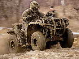 A man covered in mud, driving a quad bike