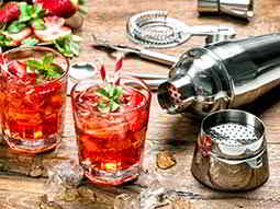 Two cocktails, freshly made, with cocktail making ingredients lying out on a wooden table 