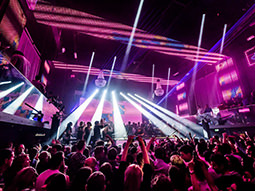 A large crowd in a nightclub that has purple decor and strobe lights