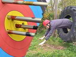 A split image of an archery target with arrows in it and a person jumping through a large tyre
