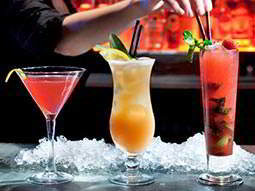 A row of three different cocktails in front of a pile of crushed ice