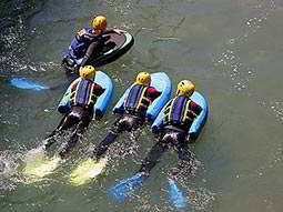 A group of people paddle through water, holding onto floats