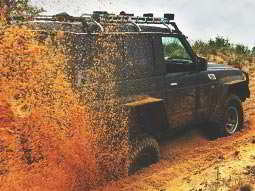 A 4x4 vehicle with its rear wheels bogged down, spraying orange muddy water out behind it