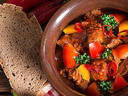 Some traditional food in a brown bowl, with some bread lying next to it 