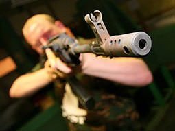 A man wearing camouflage and aiming his gun just beyond the camera
