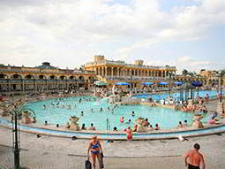 The exterior pool of Szechenyi Thermal Baths, crowded with people, with buildings in the background