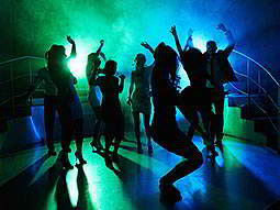Silhouettes of people dancing in a club, under green and blue disco lighting 