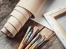An artist's paint brushes and canvas laid out on a wooden table 
