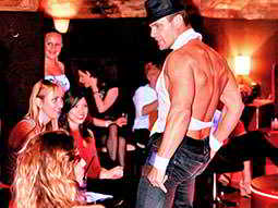 A male stripper in jeans, standing in front of a group of women sat down