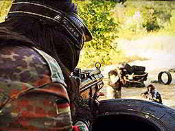 A person wearing camouflage shooting their gun at two people in the distance 