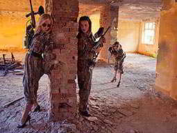 A Krakow hen group in camouflage holding paintball guns and hiding around a brick column 