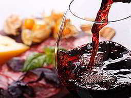 A glass of red wine being poured with food in the background