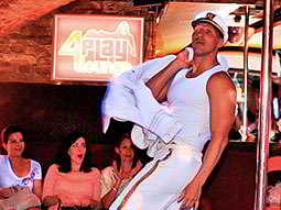 A man dressed as a pilot in a white uniform, performing on stage with women looking on