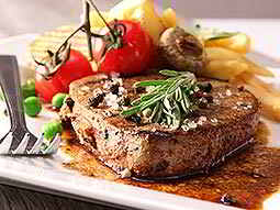 A steak topped with leaves and sea salt, with chips and tomatos in the background