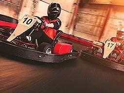 Close up on the front of two people, racing on an indoor track in go karts