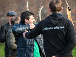 A man aiming a bow at a target with help from someone at archery