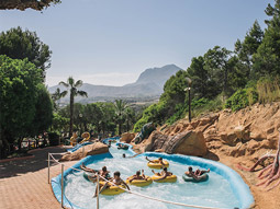 People on rubber dinghys going down a lazy river with a view of mountains at at Aqualandia Water Park in Benidorm