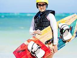 Woman holding a colourful wakeboard to a backdrop of the sea