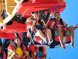 People sat screaming in a red rollercoaster to a backdrop of the sky