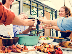 Six people sitting on a picnic bench outside, eating food and drinking from bottles