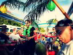 An open topped bus tour with men sat on the deck and palm trees in the foreground