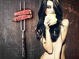 Two pieces of uncooked meat on a BBQ skewer and a naked girl eating a burger