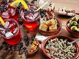Split image of red cocktails topped with lemons and ice, and Spanish tapas dishes on a table