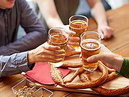 Three men raise glasses of beer together over a platter of pretzels