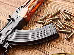 A Kalashnikov style rifle lying on a wooden table with ammunition scattered nearby