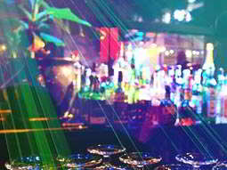 Glasses in the foreground with bottles of spirits on a bar top in the background