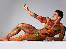 A man reclining on the floor whilst covered in paint and holding his arm up