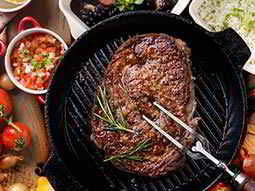 A large steak in a cast iron skillet, being stabbed with a carving fork